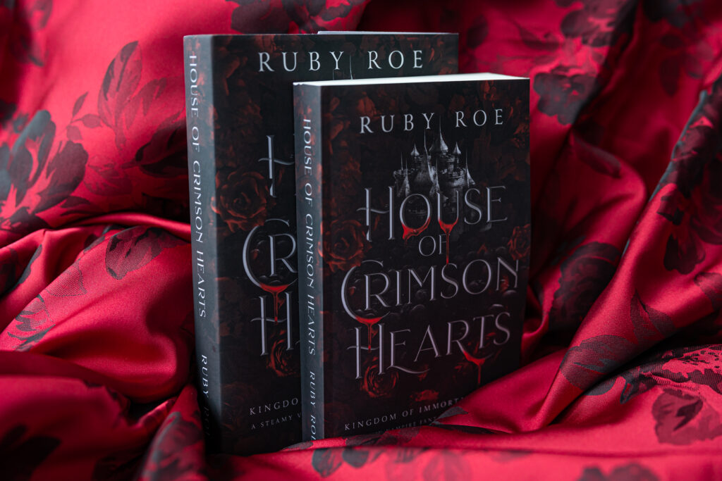 Image of the hardback and paperback books stood up on a ruffled blanket of red fabric